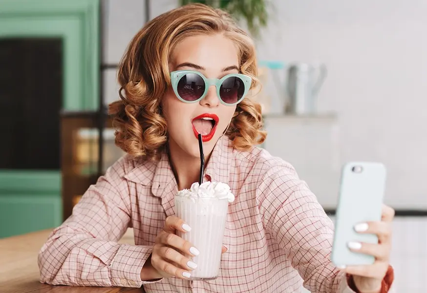 A woman holding a shake and taking a selfie