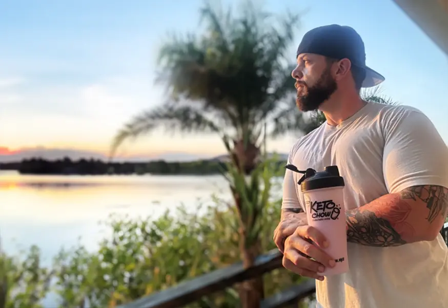 a man looking at a susnset while holding a keto chow shake