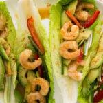 Close up - Lettuce leaves topped with spicy shrimp, sliced avocado and red peppers.