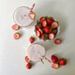 Two Strawberry Keto Chow shakes in glasses with striped straws. A bowl of strawberries sits to the side.