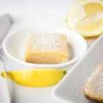 Close up - single square of Lemon Bar on a small white plate. Lemon wedges on the side.